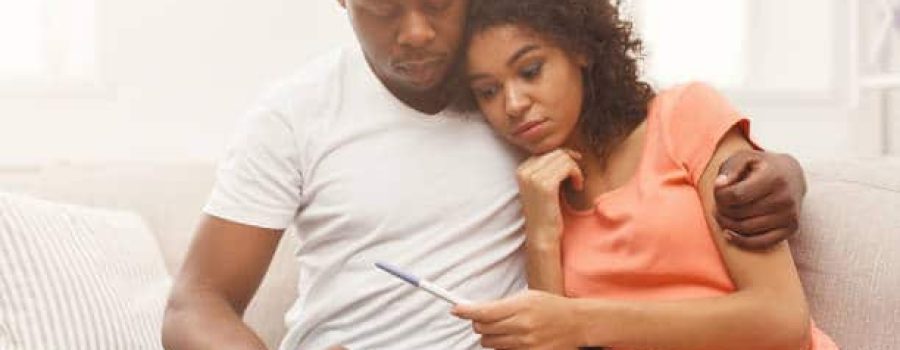 Sad african-american couple after negative pregnancy test result, sitting on couch at home, copy space