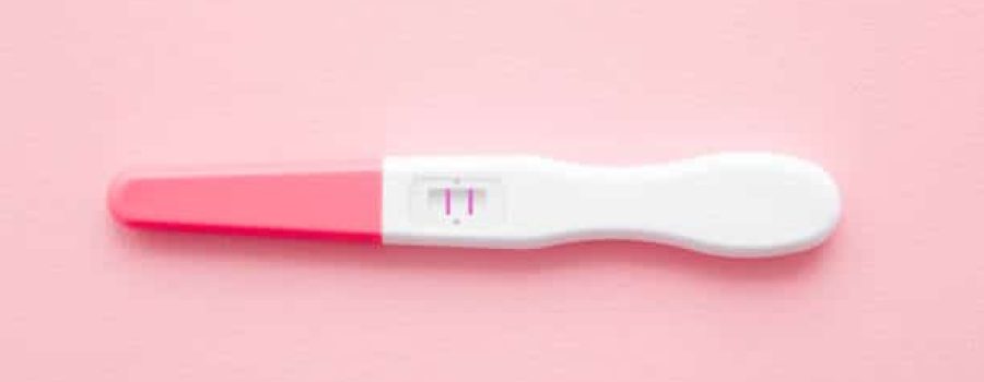 Pregnancy test with two stripes on pastel pink background. Positive result. Closeup. Top down view.