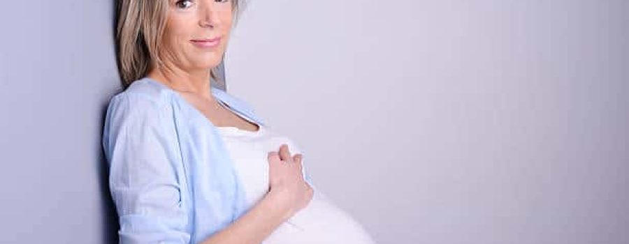 beautiful forty years old pregnant woman with blue shirt isolated on a gray background