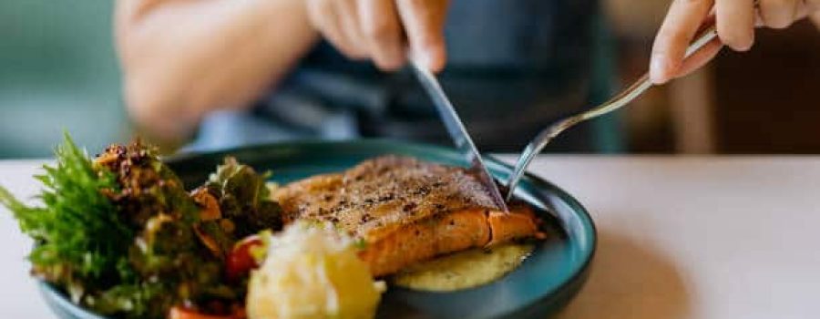 Close up shot of an Asian Chinese woman eating pan fried salmon with table knife and fork in cafe