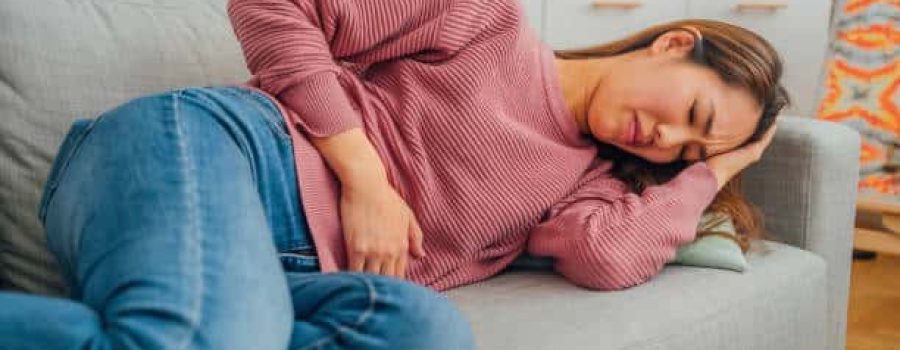 Young Japanese woman lying on her sofa alone and suffering from period cramps at home